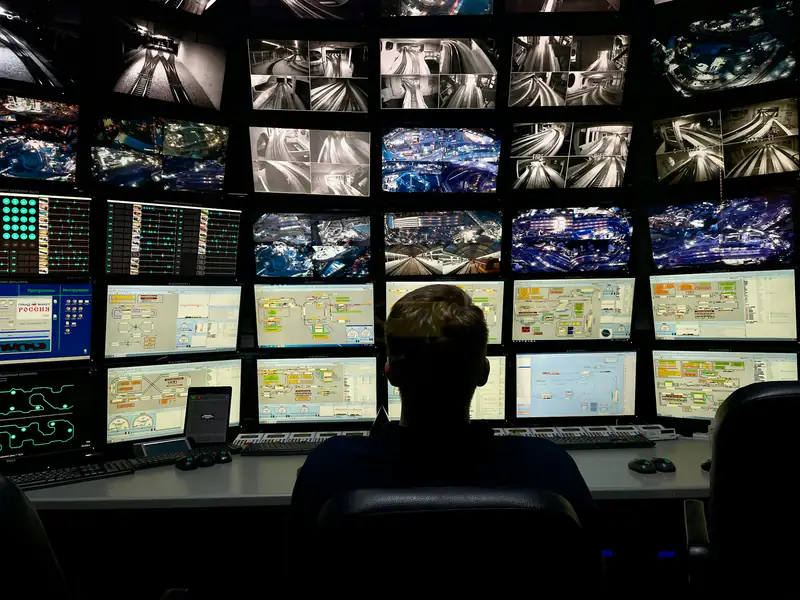 An operator seen from behind at a console, facing a wall of monitors in an operations centre.